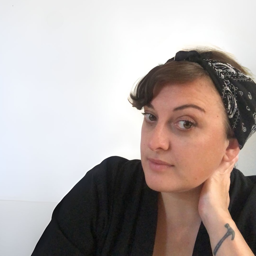 A portrait of a woman wearing a headscarf and resting a hand on her neck.