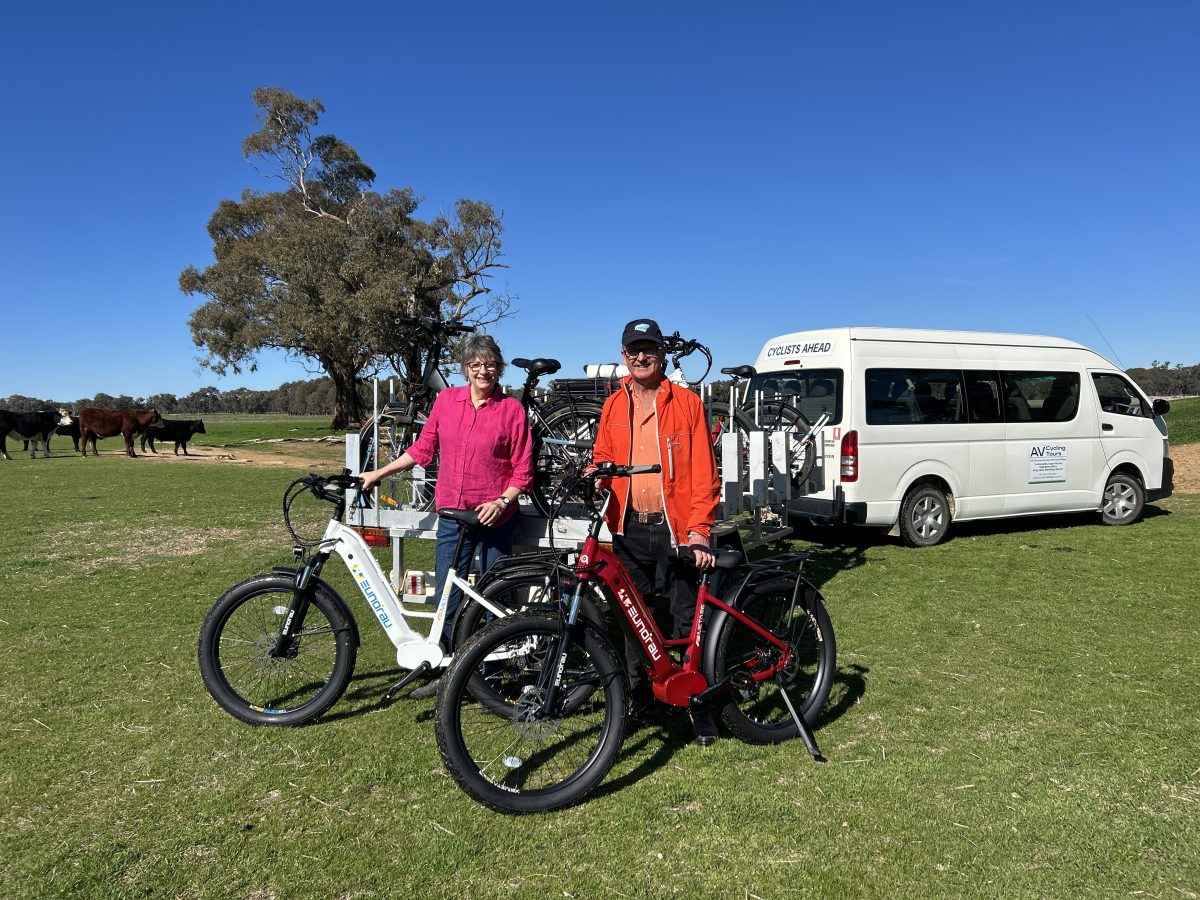 A man and a woman with electric bikes and a tour bus on a cattle farm