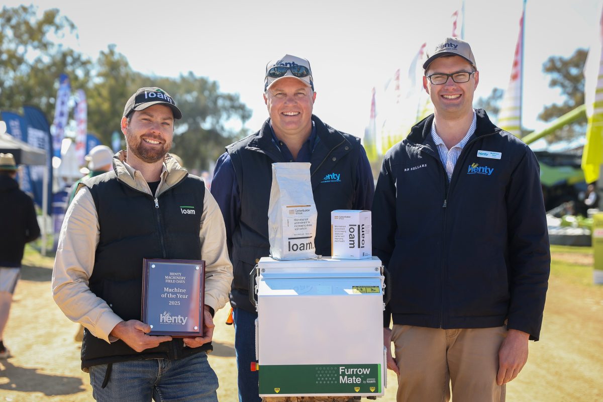 Three men standing with machine and trophy