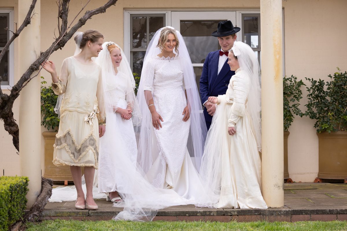 Group of young people in vintage wedding dresses stand on veranda