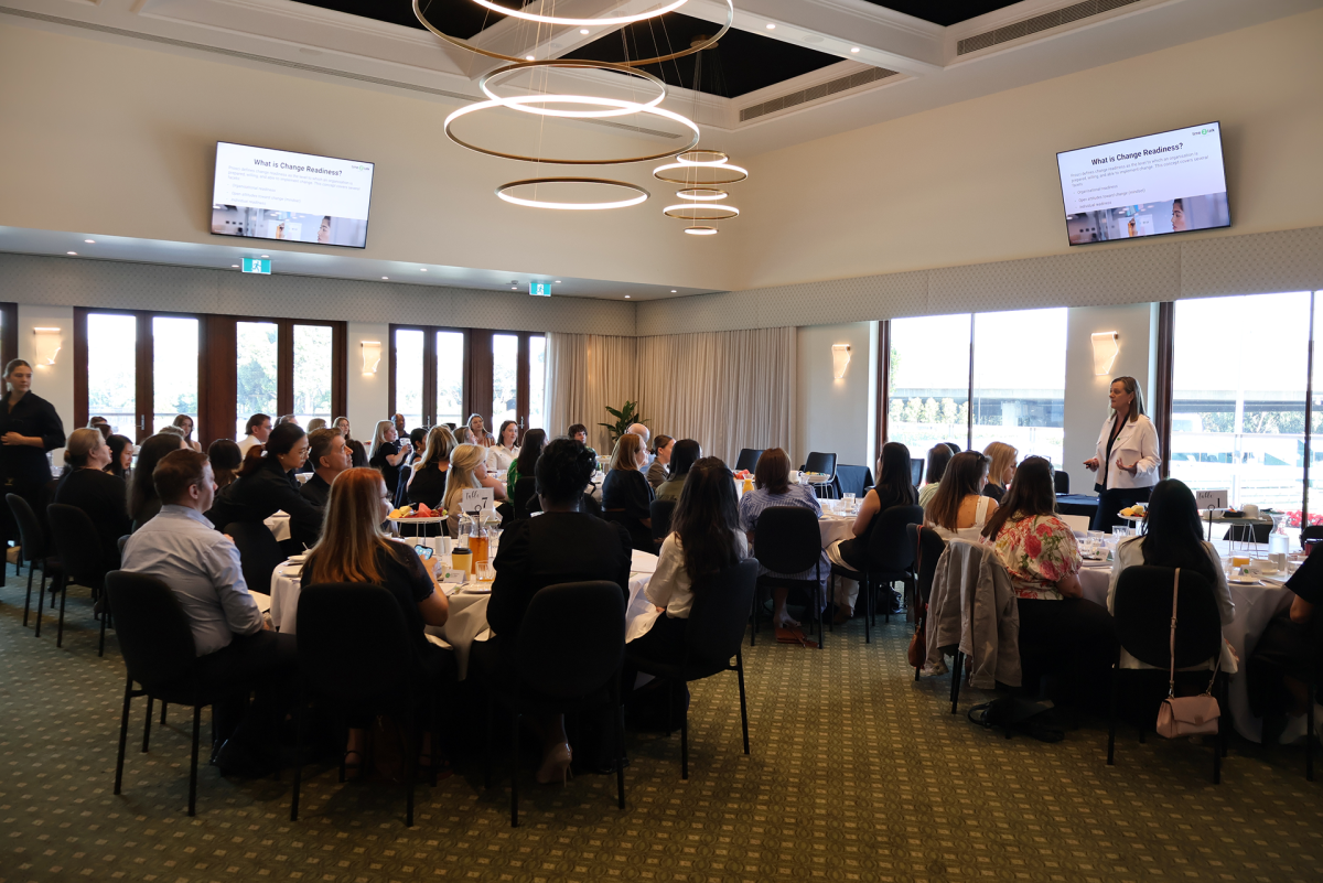a room of people at round tables listening to a person speaking