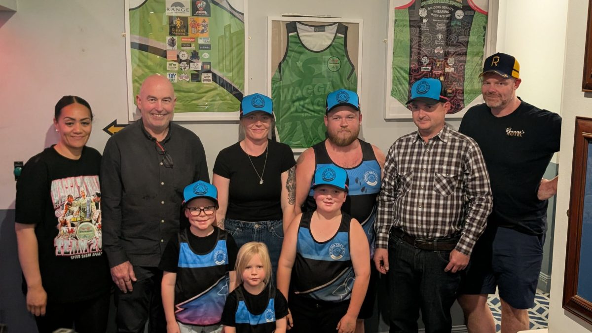 group of people standing in front of a wall of framed shirts