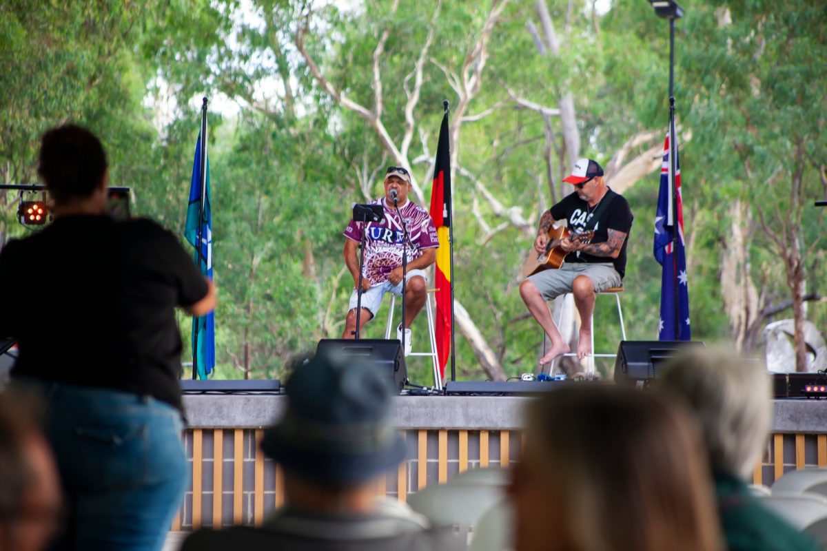 two men singing and playing guitar on a stage at an outdoor concert
